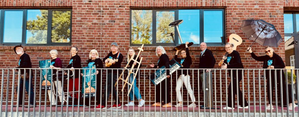 Galerie_Rieck_Meeresrausch_Eckernfoerde_Teaser Lebendiges Event‑Teaserfoto mit einer Gruppe von Personen und Musikinstrumenten vor Backsteinfassade – kreative Inszenierung für Kunst‑, Musik‑ und Mitmach‑Events.
