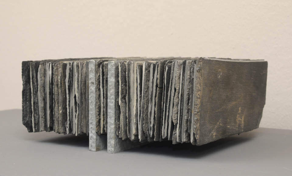 Assemblage „Schwebender Schiefer“ von Jens Chr. Jensen aus vertikal geschichteten Schieferplatten. Die skulpturale Objektkunst verbindet natürliche Materialien, Struktur und geometrische Ordnung.