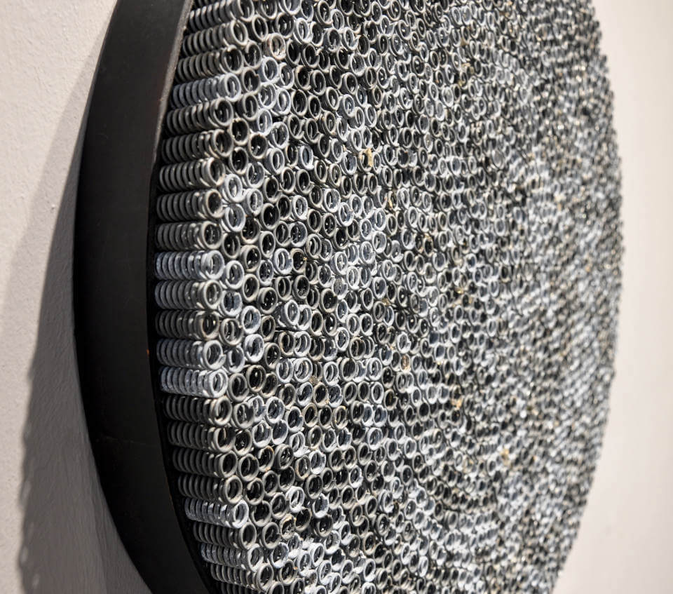 Seitliche Ansicht und Detail der runden Assemblage „Spiralen“ von Jens Chr. Jensen aus hunderten röhrenförmigen Eisenfedern. Die monochrome Wandarbeit erzeugt eine faszinierende geometrische Struktur und optische Tiefe