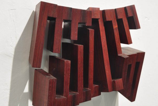 Wandobjekt „Fragiles Rot“ von Mathias Kadolph aus dunkelrotem Holz. Die geometrische Reliefskulptur erzeugt durch offene Strukturen, Tiefe und Schatten eine dynamische räumliche Wirkung.