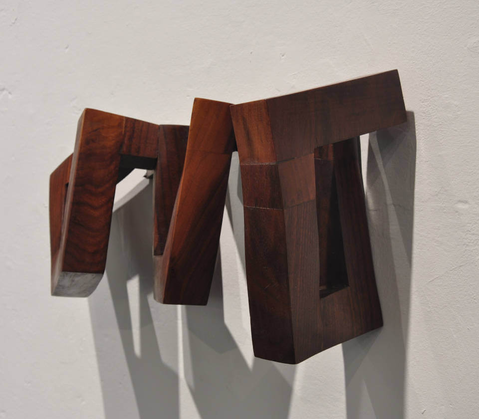 Das Werk „Trapez“ von Mathias Kadolph besteht aus mehreren miteinander verbundenen geometrischen Holzelementen. Die offenen Formen und trapezförmigen Aussparungen erzeugen eine spannende räumliche Wirkung aus Licht, Schatten und Perspektive. Die warme Holzmaserung verleiht dem Objekt eine natürliche Ausstrahlung und unterstreicht den Dialog zwischen handwerklicher Präzision und zeitgenössischer Formensprache.