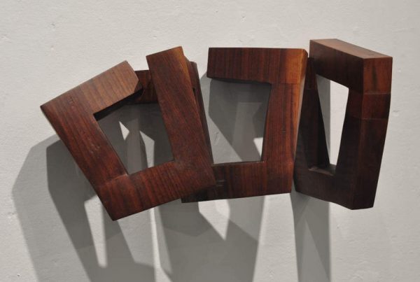 Das Werk „Trapez“ von Mathias Kadolph besteht aus mehreren miteinander verbundenen geometrischen Holzelementen. Die offenen Formen und trapezförmigen Aussparungen erzeugen eine spannende räumliche Wirkung aus Licht, Schatten und Perspektive. Die warme Holzmaserung verleiht dem Objekt eine natürliche Ausstrahlung und unterstreicht den Dialog zwischen handwerklicher Präzision und zeitgenössischer Formensprache.