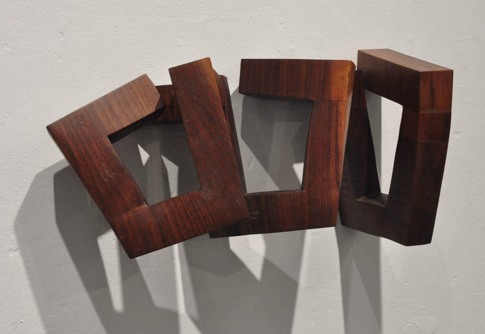 Das Werk „Trapez“ von Mathias Kadolph besteht aus mehreren miteinander verbundenen geometrischen Holzelementen. Die offenen Formen und trapezförmigen Aussparungen erzeugen eine spannende räumliche Wirkung aus Licht, Schatten und Perspektive. Die warme Holzmaserung verleiht dem Objekt eine natürliche Ausstrahlung und unterstreicht den Dialog zwischen handwerklicher Präzision und zeitgenössischer Formensprache.